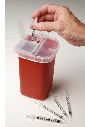 Photo of a needle being injected into a red sharps container