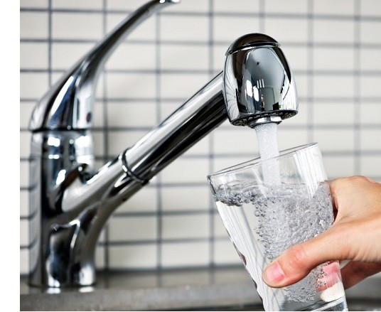 A hand filling a glass of water from a kitchen faucet