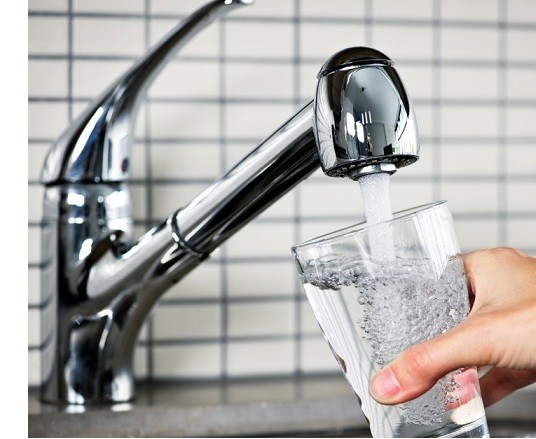 Filling a drinking glass with water from a kitchen faucet.