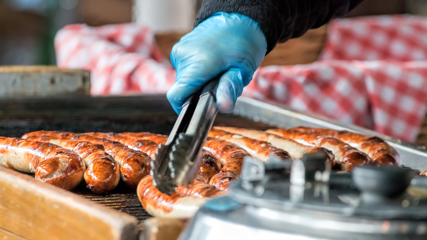 Brats being cooked on a grill at a temporary food booth.