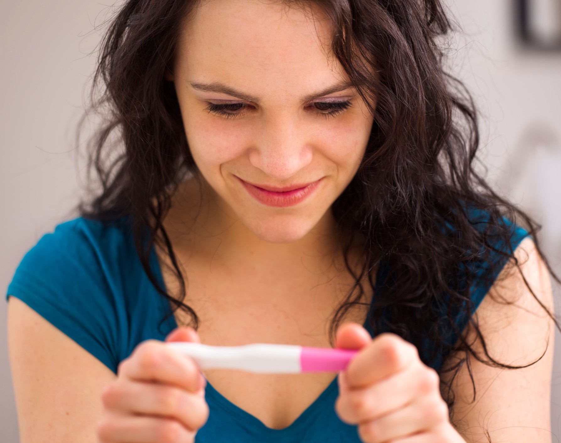 Closeup of a young woman smiling at the results of a pregnancy test. 