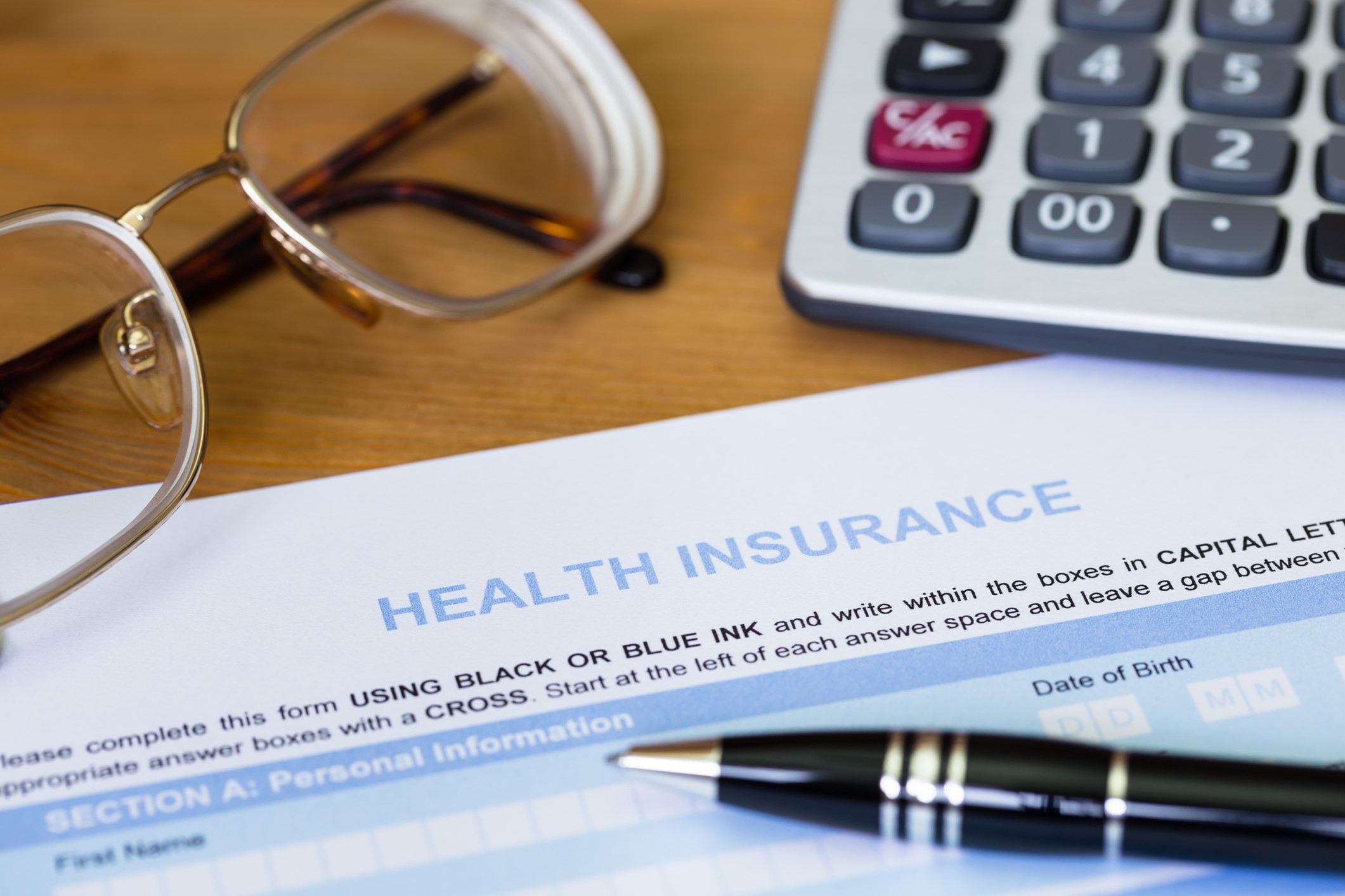 A health insurance form on a desk, with a pair of reading glasses, a calculator, and a black pen around it.